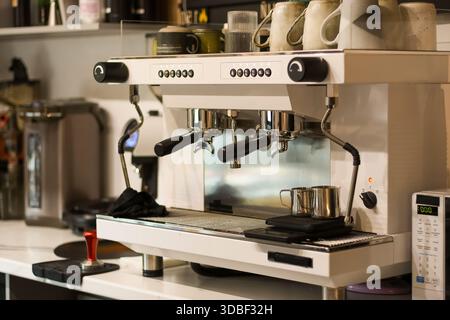 Macchina per caffè commerciale bianca sul bancone con tazze, bilancia, antimanomissione e ripiani sullo sfondo che tengono vasi e contenitori in un ambiente da caffè. Foto Stock