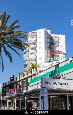 Urban Street Scene con ristoranti e Un moderno edificio di appartamenti sotto Un cielo azzurro a Los Cristianos, Tenerife. Foto Stock