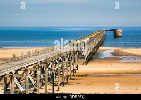 Un lungo molo in legno si estende attraverso Una spiaggia sabbiosa nell'Oceano sotto Un cielo blu a Steetley Pier, Regno Unito. Foto Stock