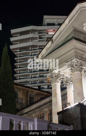 Vista notturna delle colonne classiche che circondano un edificio di appartamenti contemporaneo, circondato da alberi. Foto Stock