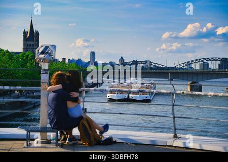 Coppia romantica che abbraccia il lungofiume Promenade con vista sulla Cattedrale di Colonia e sul Ponte Hohenzollern con navi da crociera sul fiume Reno Foto Stock