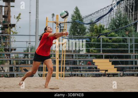 Giocatrice di pallavolo in camicia rossa si tuffa per salvare la palla sul campo da Beach volley all'aperto Foto Stock