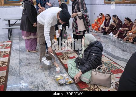 In una cucina comune laangar del tempio Sikh un volontario versa il tè e interagisce con una donna anziana in un cappotto. Nel Queens, New York, un posto diverso. Foto Stock