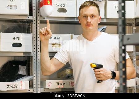 Il membro del personale tiene il dispositivo e punta il dito verso l'alto in mezzo ai ripiani Foto Stock
