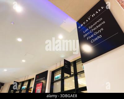 Stretford, Regno Unito - 15 novembre 2025: Moderno corridoio al coperto a Manchester con cartellonistica luminosa, porte di vetro e ambiente calmo e illuminato dal blu. Foto Stock