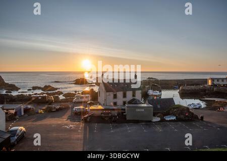 Tramonto dorato sul villaggio costiero di St Abbs, barche nel porto, costa rocciosa oggi. Foto Stock