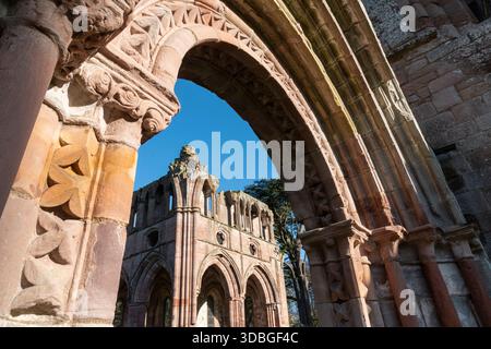 L'antico arco dell'abbazia di Dryburgh presenta sculture in pietra ornate e archi intemprati contro un cielo limpido. Foto Stock
