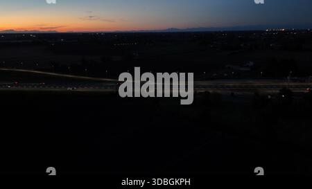 Il traffico dell'autostrada A21 che scorre di notte sull'autostrada Brescia Piacenza, auto e camion si spostano lungo una strada illuminata con uno skyline urbano e una foce Foto Stock