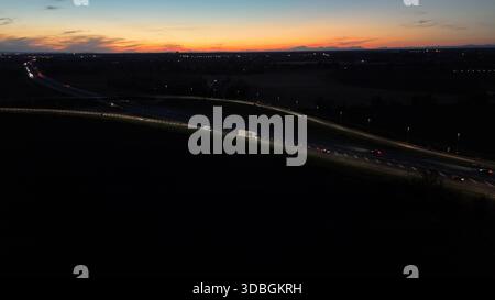 Vista aerea notturna che mostra il traffico intenso sull'autostrada A21 Piacenza Brescia al tramonto, auto e camion che si muovono lungo la strada illuminando con l Foto Stock