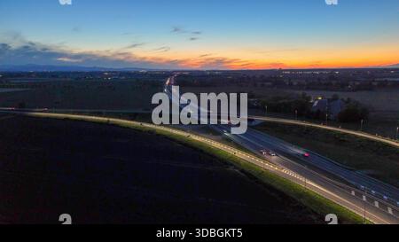 Traffico autostradale percorrendo l'autostrada A21 nei pressi di Piacenza Brescia di notte, veicoli che creano sentieri leggeri sulle infrastrutture e sulla rete stradale durante il sottopassaggio Foto Stock