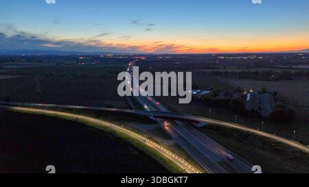 Autostrada A21 che mostra il flusso del traffico serale, veicoli che si muovono lungo l'autostrada illuminata e strade di cavalcavia che collegano città lontane sotto un bellissimo stato Foto Stock