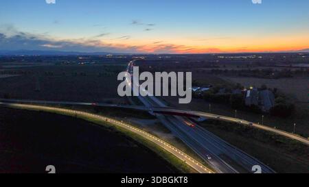 Autostrada A21 che mostra il flusso del traffico serale, veicoli che si muovono lungo l'autostrada illuminata e strade di cavalcavia che collegano città lontane sotto un bellissimo stato Foto Stock