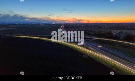 Autostrada A21 che mostra il flusso del traffico serale, veicoli che si muovono lungo l'autostrada illuminata e strade di cavalcavia che collegano città lontane sotto un bellissimo stato Foto Stock
