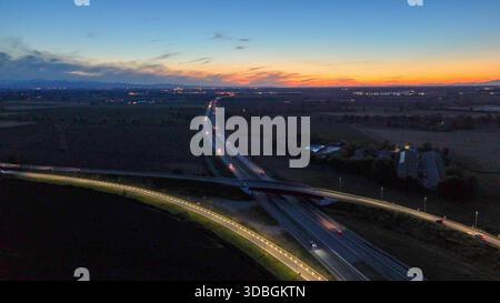 Autostrada A21 che mostra il flusso del traffico serale, veicoli che si muovono lungo l'autostrada illuminata e strade di cavalcavia che collegano città lontane sotto un bellissimo stato Foto Stock