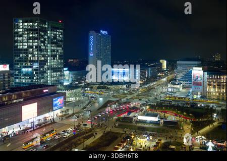 Vista aerea notturna del centro di Varsavia con grattacieli illuminati, strade trafficate e luci della città, tra cui la rotonda romana Dmowski e l'hotel Novotel. Foto Stock