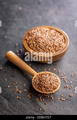 Semi di lino o di lino. Sano seme di lino su un cucchiaio di legno su un tavolo nero. Foto Stock