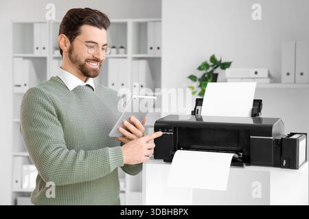 Bell'uomo con un tablet che usa una stampante in ufficio Foto Stock