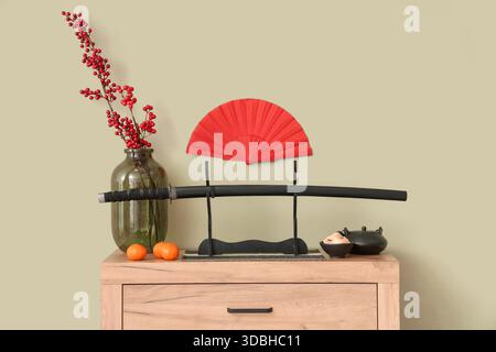 Katana con teiera, tè giapponese e decorazioni su comò vicino al muro verde. Festa di Capodanno Foto Stock