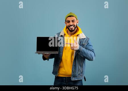 Young Man sfoggia un notebook su sfondo blu con un abbigliamento casual Foto Stock