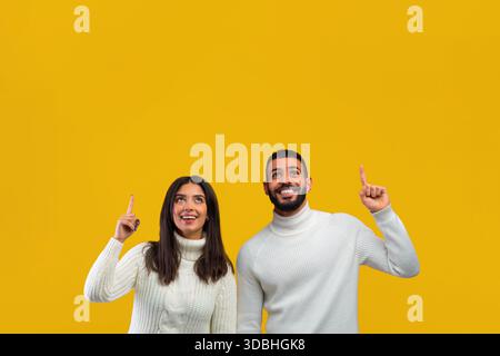 Giovane coppia che punta con gioia verso l'alto su uno sfondo giallo brillante Foto Stock