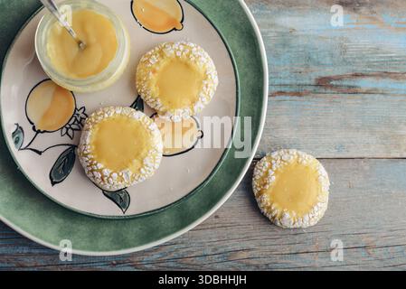 Biscotti al limone con cagliata di limone su piatto verde su fondo di legno con limoni freschi, vista dall'alto Foto Stock