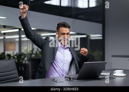 Celebrazione del successo nel moderno spazio ufficio con Man Raising Fist e sorridente Foto Stock