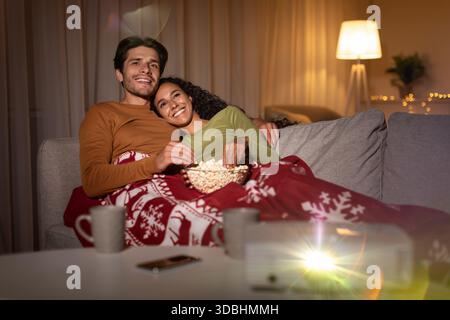 Una coppia felice si diverte con i film di Natale e con i popcorn nell'accogliente serata invernale Foto Stock