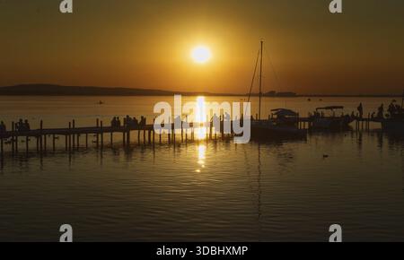 Tramonto sullo Steinhuder Meer con gente su un molo, che riflette le barche a vela, tranquillo, Steinhude Foto Stock