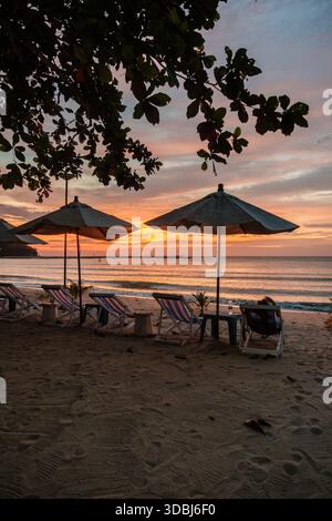 Scena rilassante alla spiaggia di Baan Krood in Thailandia durante il tramonto. Ombrelli colorati offrono ombra su comodi lettini, invitando i visitatori a godersi la tranquilla riva e il cielo vivace. Foto Stock