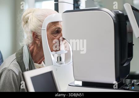 Donna caucasica anziana sottoposta a esame oculistico utilizzando oftalmologia macchina diagnostica in clinica medica Foto Stock