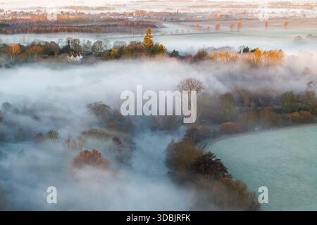 Vista aerea di un paesaggio avvolto da nebbia eterea, dove sagome di alberi e luce dorata perforano la nebbia, la valle del Tamigi, l'Oxfordshire, Unit Foto Stock