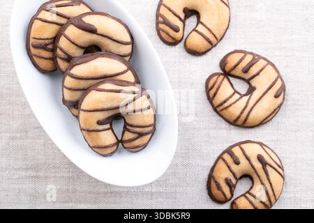 Biscotti di pasta frolla a forma di mezzaluna, in una ciotola bianca su lino. Biscotti friabili, a base di burro, zucchero e farina. Foto Stock