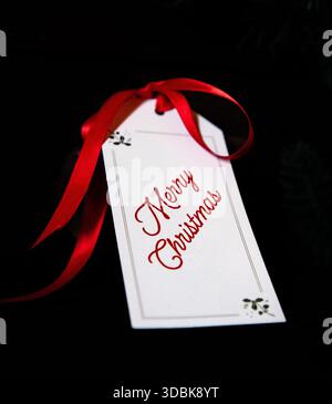 Un nastro rosso legato all'etichetta natalizia "buon Natale" Foto Stock