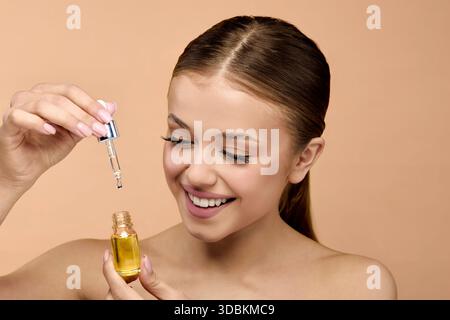 Donna tiene il flacone contagocce con siero e sorride mentre applica il prodotto per la cura della pelle per una pelle sana in ambiente studio. Questo momento cattura l'attenzione su B. Foto Stock