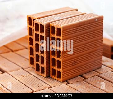 Diversi mattoni cavi in terracotta sono impilati ordinatamente su un pallet di legno in un cantiere, pronti per essere utilizzati nella costruzione di una nuova struttura Foto Stock