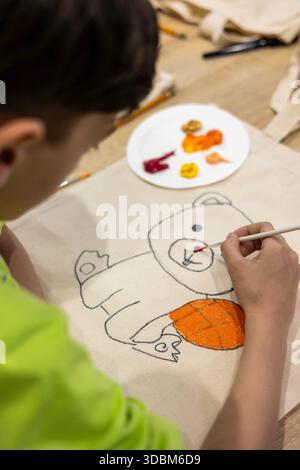 Bambini che dipingono su una borsa di tela durante un laboratorio creativo di arte terapia. Artigianato ecologico per bambini: Dipingere borse tote riutilizzabili in un'arte sostenibile Foto Stock