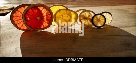 Vari agrumi secchi retroilluminati su legno con ombre. Consistenza di frutta visibile con motivi naturali per le decorazioni natalizie. Foto Stock