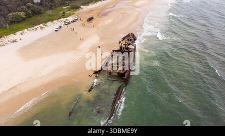 Vista aerea del relitto arrugginito della SS Maheno che giace sulla spiaggia, dove la sabbia dorata incontra l'acqua turchese, Fraser Island, Queensland, A. Foto Stock