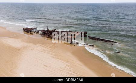 Vista aerea del relitto della SS Maheno che riposa sulla spiaggia sabbiosa, un netto contrasto con il mare turbolento, Fraser Island, Queensland, Australia. Foto Stock