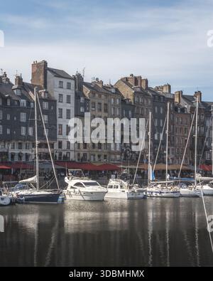 Vista delle barche che rimbalzano dolcemente nell'acqua mentre edifici colorati si ergono alti sotto un cielo limpido, creando una scena pittoresca, Honfleur, Normandia, Francia Foto Stock