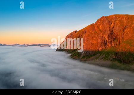 Vista aerea delle nuvole basse che si muovono intorno a una montagna e sopra la città di Eggum al sole di mezzanotte in estate. Eggum Unstad, Vestvagoy Lofoten, Isole, Norvegia, Europa. Foto Stock