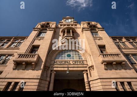 Veduta di un grande edificio dell'ufficio municipale con la sua torre dell'orologio che raggiunge il cielo blu, catturato da un angolo basso, Karachi, Sindh, Pakistan. Foto Stock
