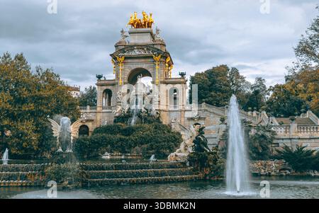 La vista delle acque a cascata scorre dalla monumentale fontana, figure dorate che brillano in cima ad archi di pietra in mezzo al verde, un'oasi serena, Barcellona Foto Stock
