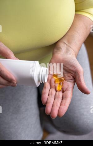 Mani anziane che versano capsule dorate dal vaso per pillole bianco. Salute in età adulta, mantenendo attività ed energia. Prevenzione delle malattie, uso di vitamine AN Foto Stock