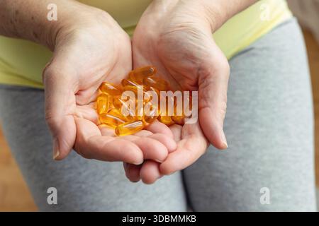 Mani che invecchiano che tengono le capsule dorate. Salute in età adulta, mantenendo attività ed energia. Prevenzione delle malattie, uso di vitamine e integratori, trattamento Foto Stock