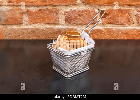 Churros al cioccolato, realizzati con impasto a base di cacao, fritti e cosparsi di zucchero a velo e scaglie di cioccolato, serviti con cioccolata calda e frusta Foto Stock