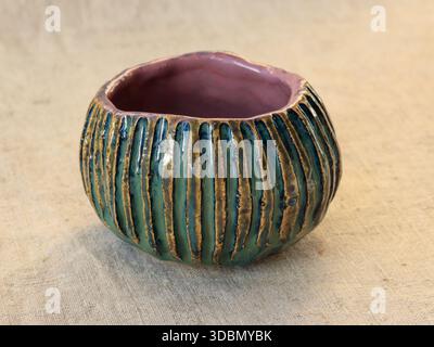 Recipiente in ceramica realizzato a mano con nervature verticali e smalto verde lucido, fotografato su tessuto di lino naturale. Natura morta minimalista che mette in risalto l'ar Foto Stock