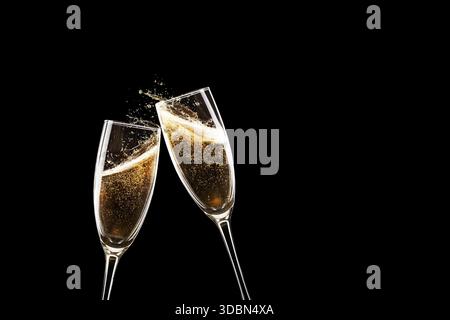Due flauti di champagne con brindisi natalizi. Le bolle d'oro e gli spruzzi su Uno sfondo nero drammatico. Elegant Celebration, Capodanno o W. Foto Stock