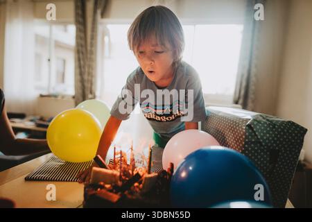 Ragazzo di fronte alla sua torta di compleanno con candele accese Foto Stock