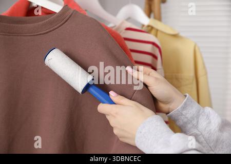 Donna che pulisce la felpa con rullo di lanugine a casa, primo piano Foto Stock